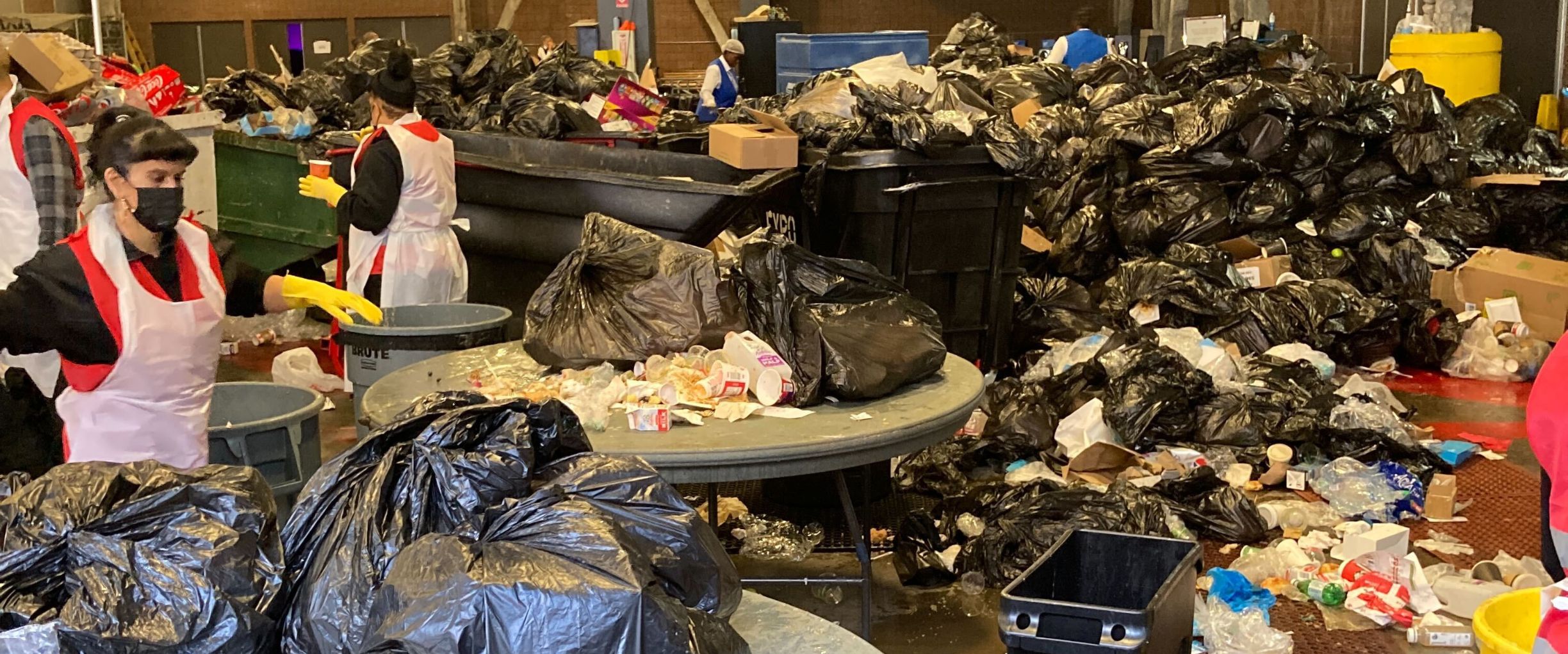 A room full of trash, recycles, and compost workers in aprons sorting