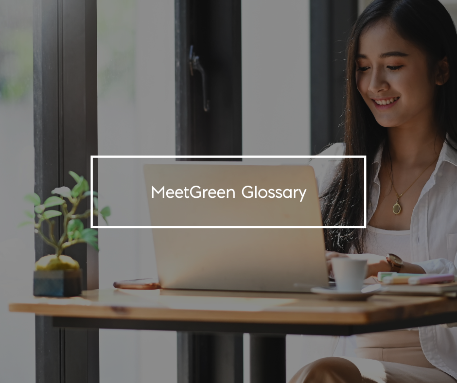 A woman sitting in front of a laptop working Text: MeetGreen Glossary